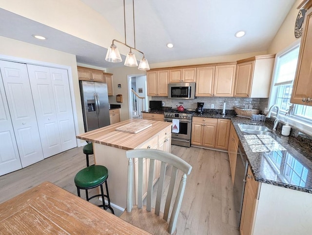 kitchen featuring stainless steel appliances, butcher block countertops, a sink, a kitchen breakfast bar, and backsplash