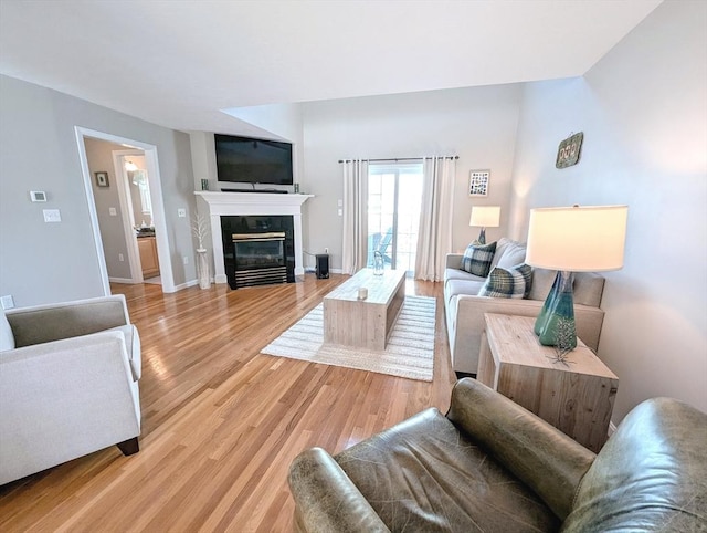 living area with light wood finished floors, a fireplace with flush hearth, and baseboards