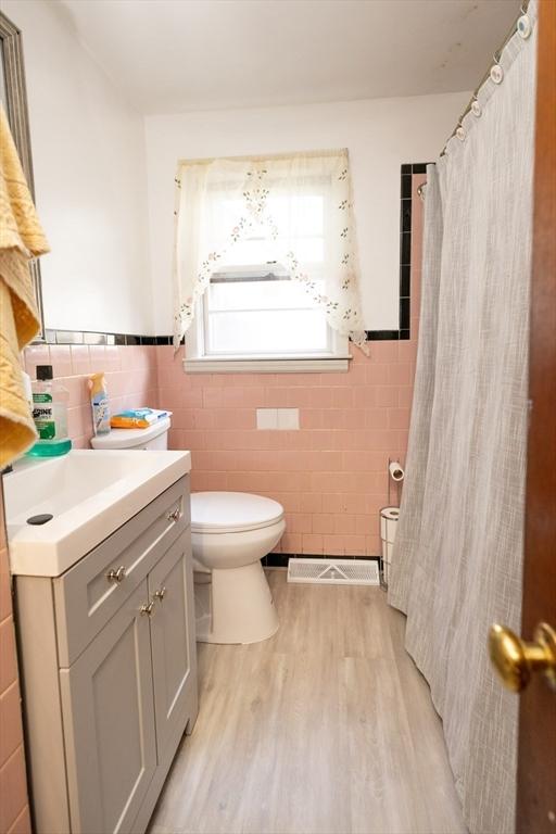 bathroom with toilet, tile walls, wood-type flooring, vanity, and curtained shower