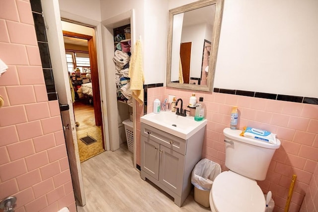 bathroom with toilet, tile walls, wood-type flooring, and vanity