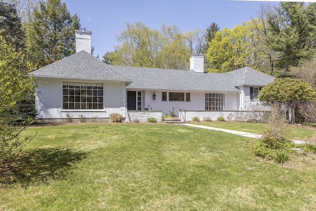 rear view of house featuring a chimney, a lawn, and roof with shingles