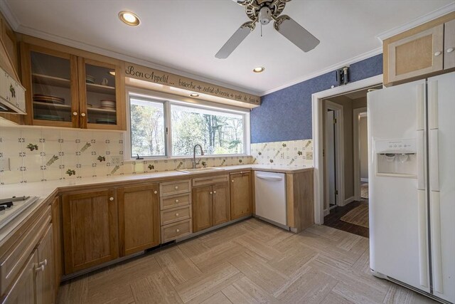 kitchen with white appliances, a sink, light countertops, ornamental molding, and brown cabinetry