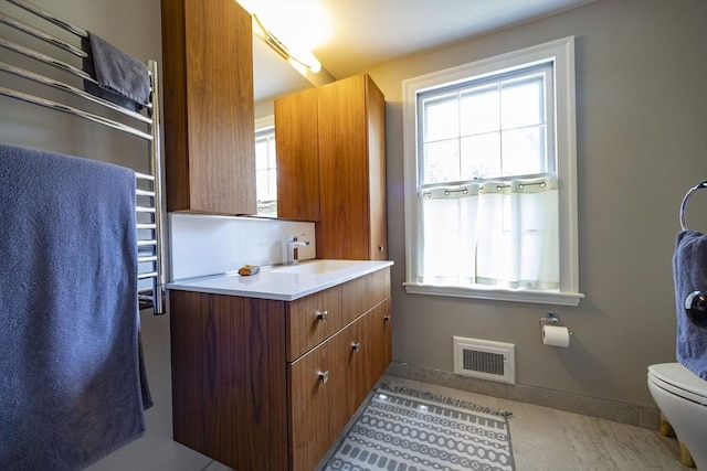 bathroom with baseboards, vanity, toilet, and a towel warming rack