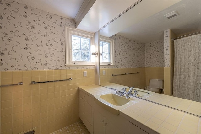 bathroom featuring wallpapered walls, tile walls, toilet, a wainscoted wall, and vanity
