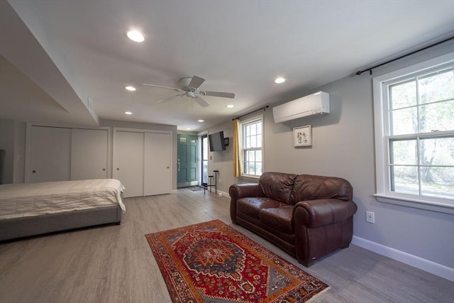 bedroom featuring an AC wall unit, light wood-style flooring, baseboards, recessed lighting, and two closets