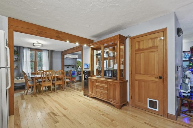 dining room with a textured ceiling, light hardwood / wood-style flooring, and a wall unit AC