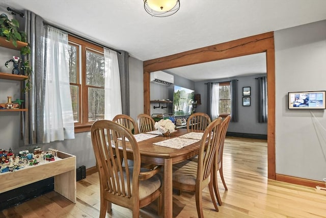 dining room with light wood-type flooring, a wall mounted air conditioner, and a wealth of natural light