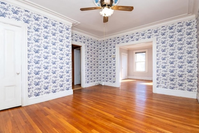 unfurnished room featuring a ceiling fan, baseboards, wallpapered walls, ornamental molding, and light wood-type flooring