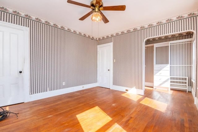 empty room with baseboards, wood finished floors, and wallpapered walls