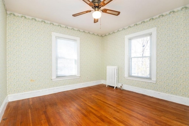 empty room with baseboards, wood finished floors, radiator heating unit, and wallpapered walls