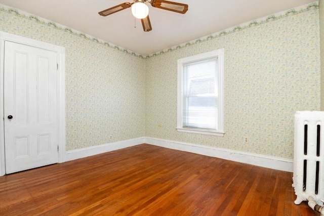 unfurnished room featuring wood finished floors, radiator heating unit, and wallpapered walls