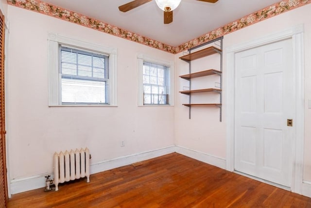 unfurnished room featuring radiator, wood finished floors, baseboards, and ceiling fan