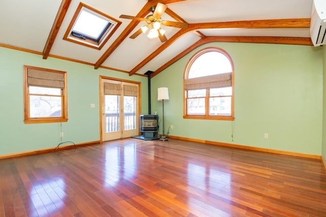 unfurnished living room with a wealth of natural light, a wood stove, ceiling fan, and wood finished floors