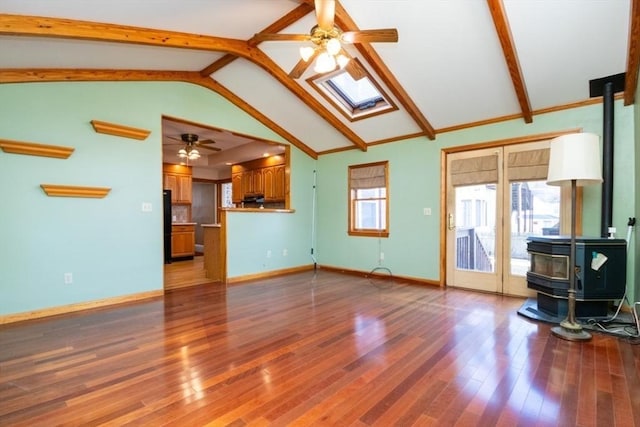 unfurnished living room with a ceiling fan, wood finished floors, vaulted ceiling with skylight, baseboards, and a wood stove