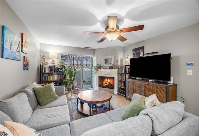 living room with light wood-type flooring, a warm lit fireplace, and ceiling fan