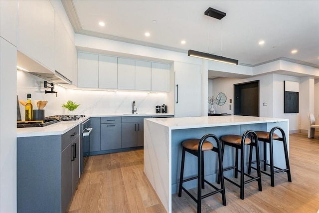 kitchen featuring decorative light fixtures, white cabinets, backsplash, a center island, and light wood-type flooring