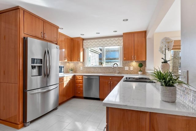 kitchen with sink, stainless steel appliances, light stone counters, backsplash, and kitchen peninsula