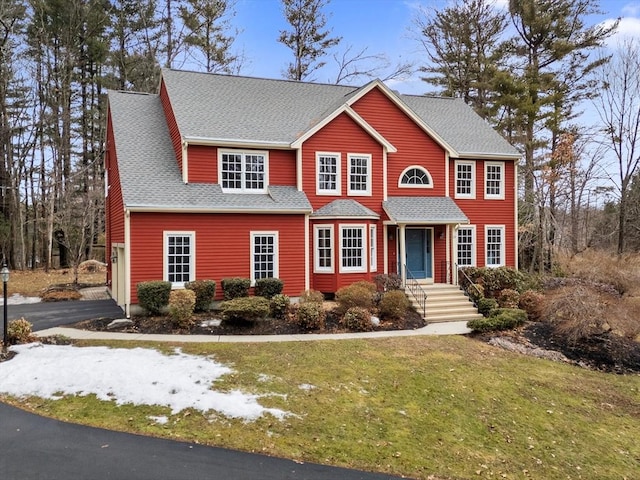 view of front facade featuring a front lawn, driveway, and roof with shingles