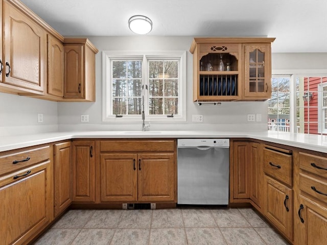 kitchen featuring a sink, glass insert cabinets, stainless steel dishwasher, and brown cabinetry