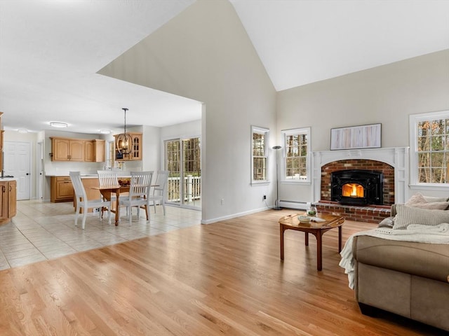 living area featuring baseboards, high vaulted ceiling, a baseboard radiator, a brick fireplace, and light wood-type flooring