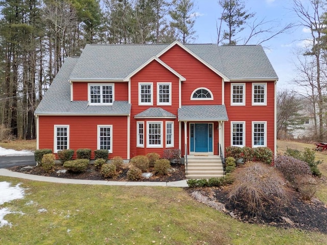 colonial home with a front yard and a shingled roof