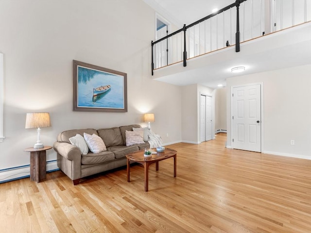 living area with light wood finished floors, baseboard heating, a high ceiling, and baseboards