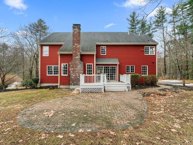 back of property with a deck, a patio, roof with shingles, and a chimney