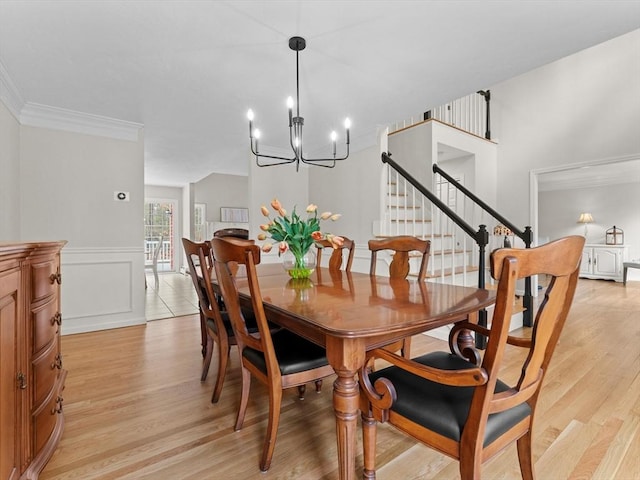 dining space with light wood-type flooring, a notable chandelier, ornamental molding, and stairway