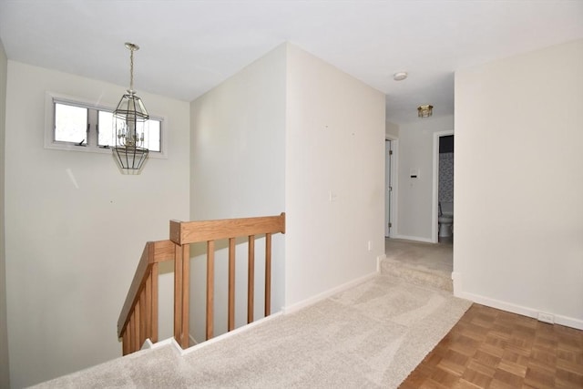 hall featuring baseboards, carpet floors, a chandelier, and an upstairs landing