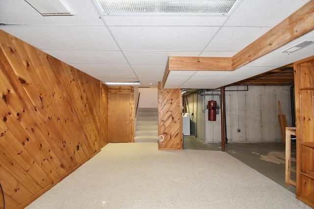 finished basement with wooden walls, washer / dryer, visible vents, and stairway