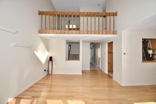 unfurnished living room with baseboards, a high ceiling, and light wood-type flooring
