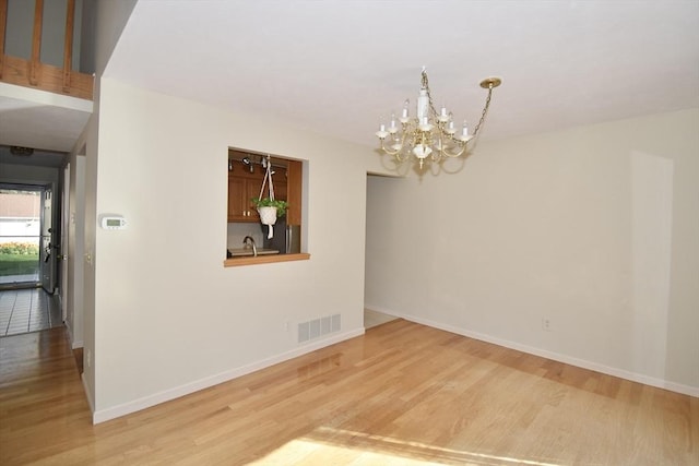 unfurnished dining area featuring a chandelier, baseboards, visible vents, and wood finished floors