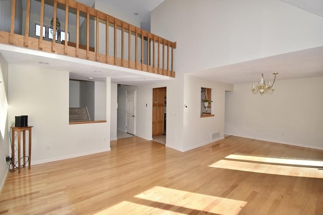 unfurnished living room with wood finished floors, stairs, a high ceiling, and a notable chandelier