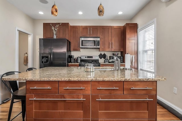 kitchen with a breakfast bar, light stone counters, a center island with sink, appliances with stainless steel finishes, and pendant lighting