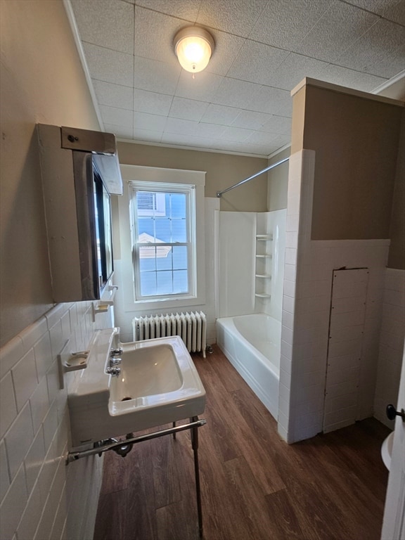 bathroom featuring sink, hardwood / wood-style flooring, radiator heating unit, shower / bathtub combination, and tile walls