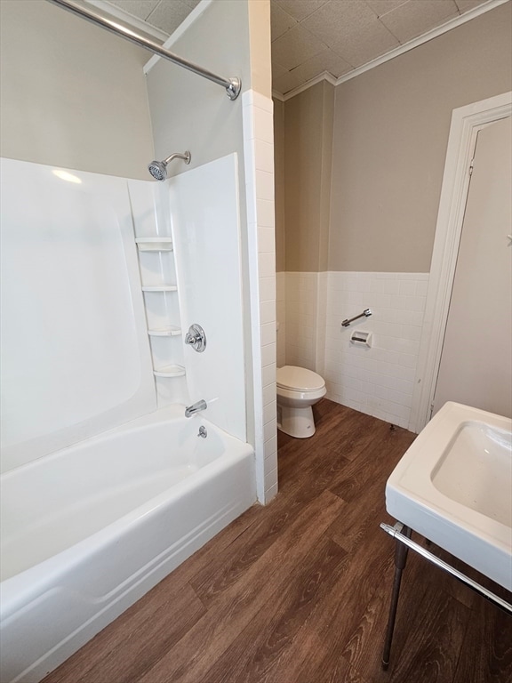 bathroom with shower / bath combination, hardwood / wood-style flooring, toilet, and tile walls