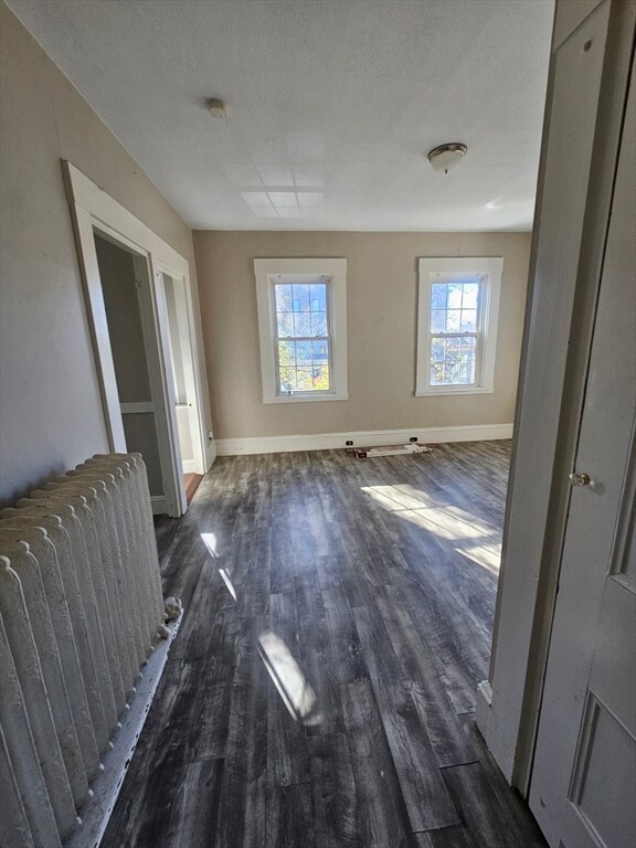 empty room with radiator heating unit, a textured ceiling, and dark hardwood / wood-style floors