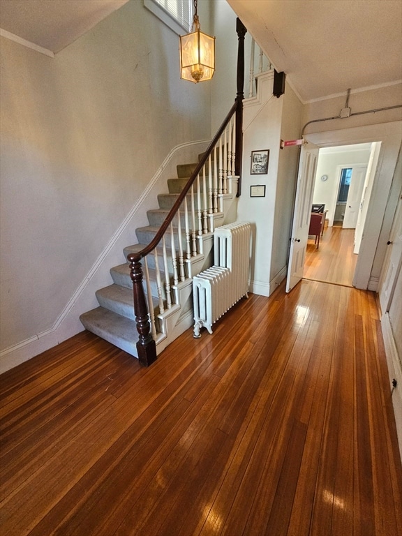 stairs featuring radiator heating unit, wood-type flooring, and crown molding