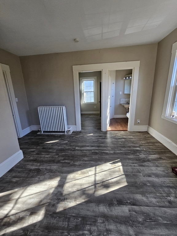 spare room featuring radiator heating unit, dark wood-type flooring, and a healthy amount of sunlight