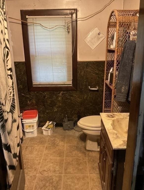 bathroom featuring tile patterned flooring, toilet, vanity, tile walls, and wainscoting