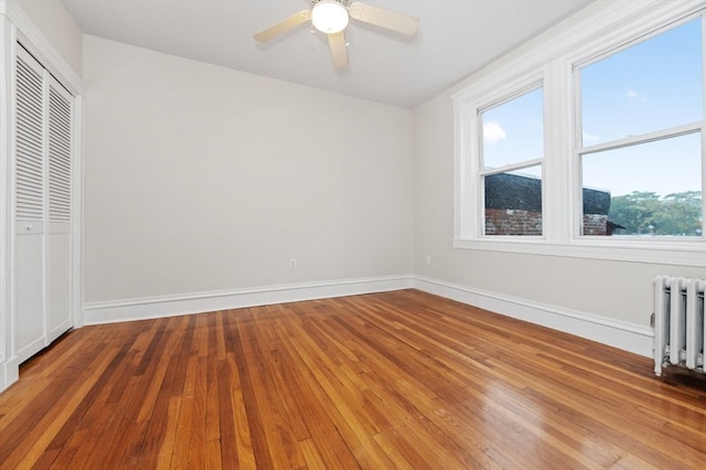 unfurnished bedroom featuring ceiling fan, a closet, radiator heating unit, and light hardwood / wood-style floors