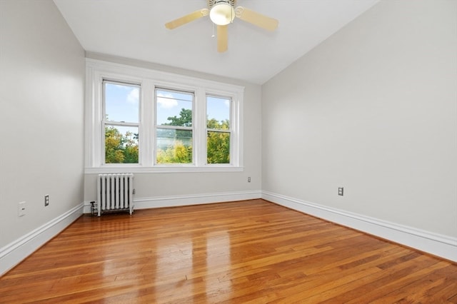 unfurnished room with ceiling fan, light hardwood / wood-style floors, vaulted ceiling, and radiator