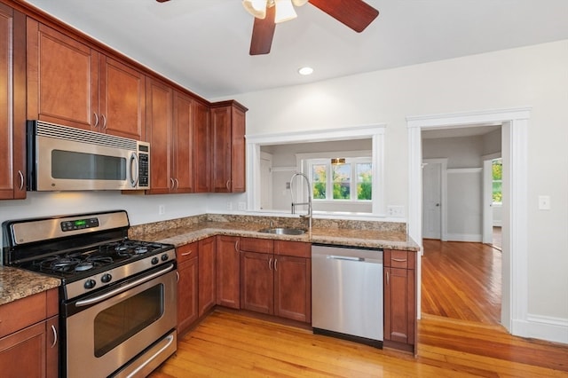 kitchen featuring light stone counters, ceiling fan, sink, light hardwood / wood-style flooring, and appliances with stainless steel finishes