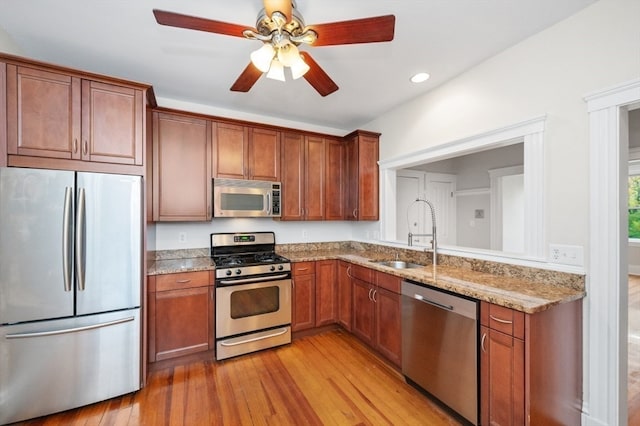 kitchen featuring light wood-type flooring, ceiling fan, sink, light stone countertops, and appliances with stainless steel finishes