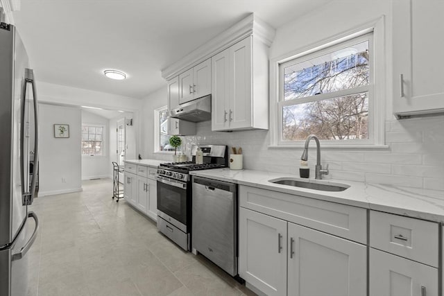 kitchen with light stone counters, stainless steel appliances, under cabinet range hood, white cabinetry, and a sink