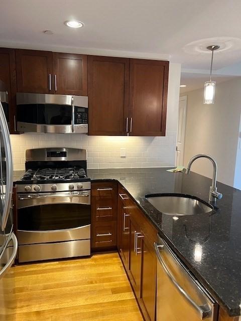 kitchen featuring decorative light fixtures, light wood finished floors, appliances with stainless steel finishes, a sink, and dark stone countertops