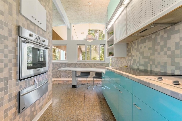 kitchen with pendant lighting, white cabinetry, backsplash, stainless steel oven, and custom range hood