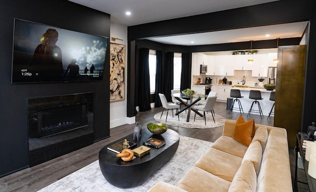 living room featuring dark wood-style flooring, baseboards, a lit fireplace, and recessed lighting
