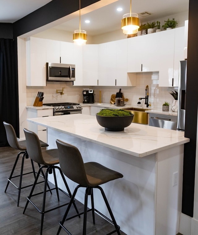 kitchen featuring stainless steel appliances, dark wood-type flooring, decorative light fixtures, and white cabinetry