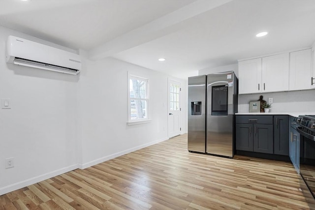 kitchen featuring stainless steel fridge, black range oven, a wall mounted AC, light hardwood / wood-style flooring, and white cabinetry